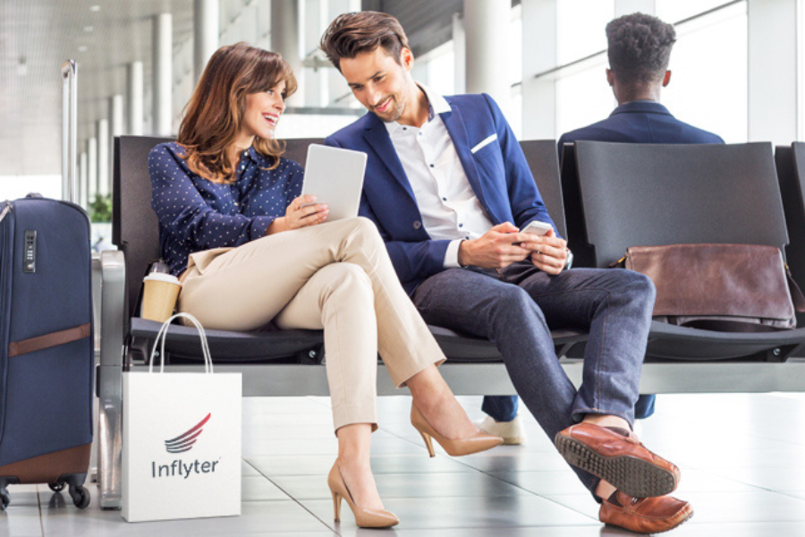 Brunette couple smiling in airport with suitcase and duty-free shopping bag