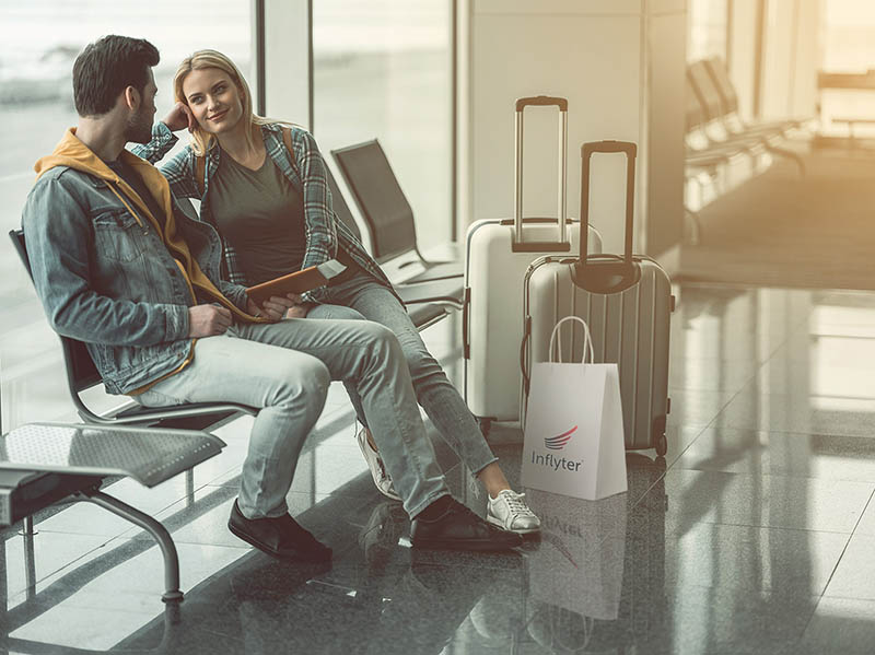 Blonde and brunette couple smiling in airport with suitcase and duty-free shopping bag