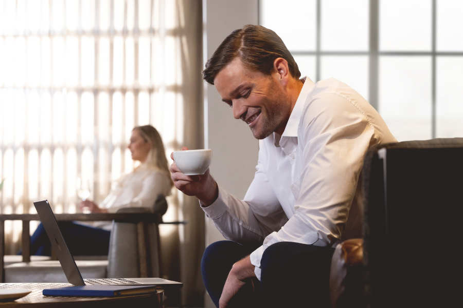 A man working on a laptop and drinking coffee at a table.