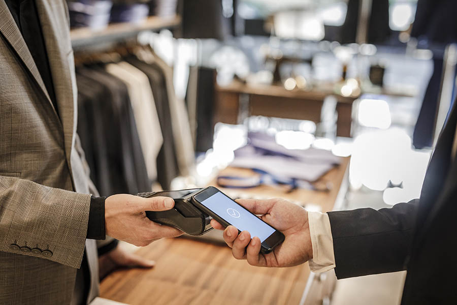 Close up of businessman using his smart phone ta pay in a store.