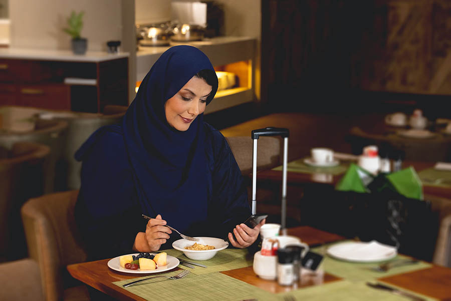 A woman in a blue hijab looking at her phone, at an airport lounge.