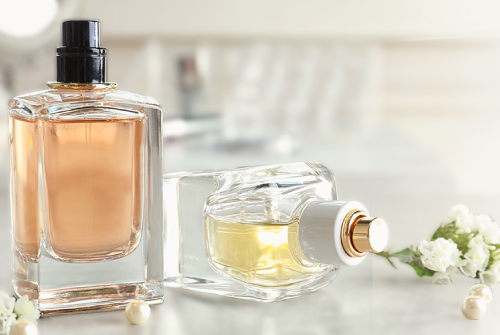 Photo of two luxury perfume bottles, one lying on its side with flowers in the background