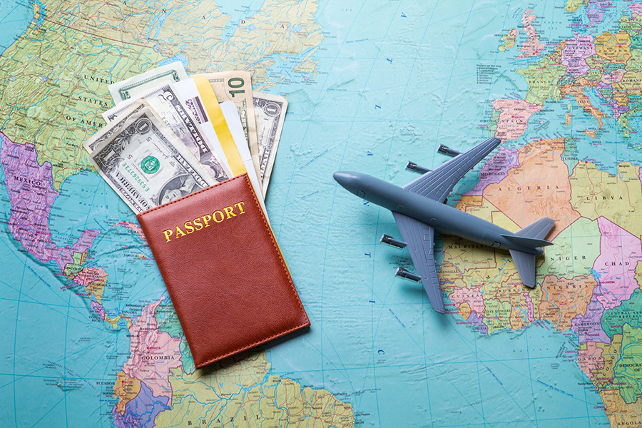 Flat lay of toy plane on a map of the world and Dollars inside a brown passport.