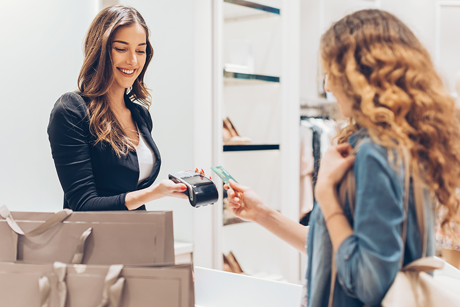 Young woman giving her credit card for a contactless payment in the fashion store
