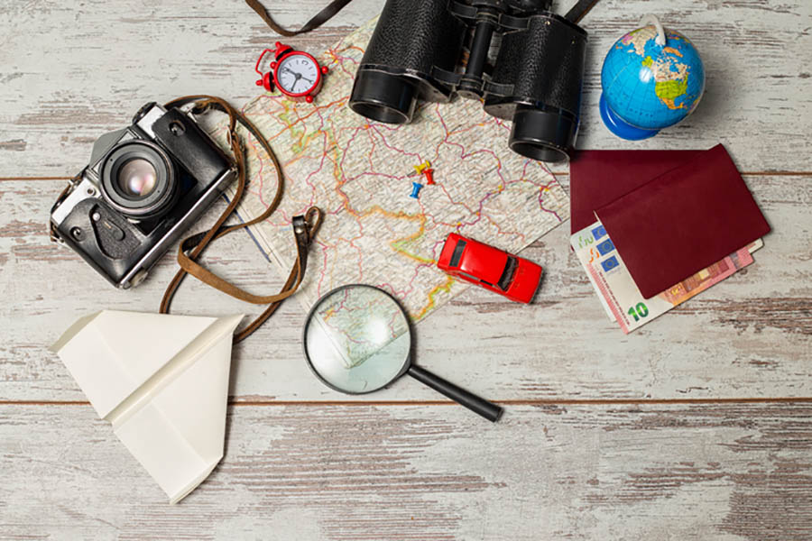 Flat lay of travelling essentials. Camera, paper plane, magnifying glass, map, binoculars and passport.